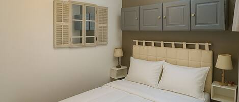 A bedroom with a bed, two bedside tables, a nightstand, a hanging light fixture, and a wardrobe.
