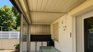 Un patio couvert comprenant une table en verre, un banc intégré et une porte coulissante donnant sur une cuisine.