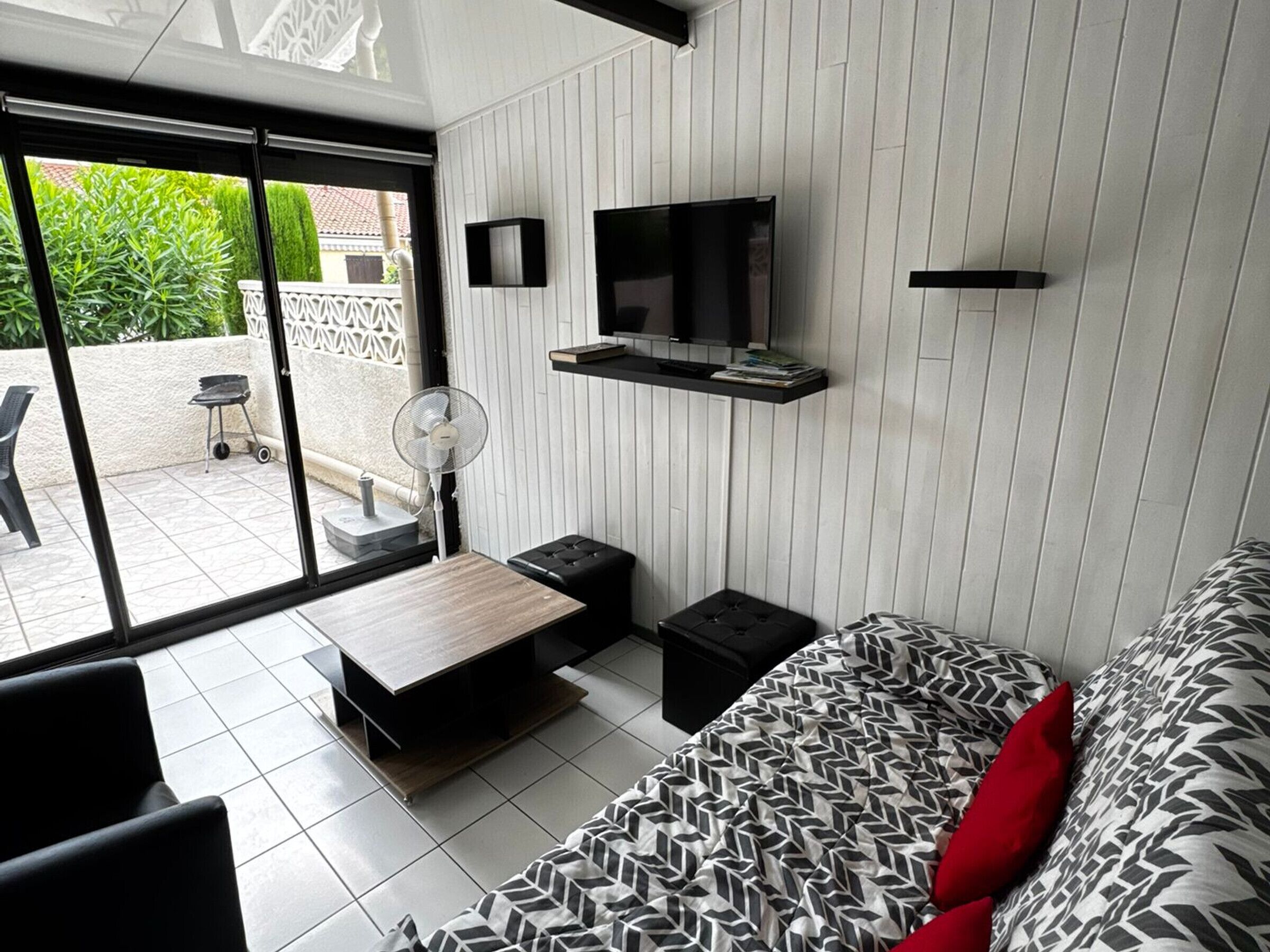 A modern living room with a sofa, a coffee table, a TV mounted on the wall, and a fan.