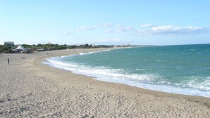 A wide sandy beach with gentle waves, a clear sky, and distant buildings. - Holiday pavilion 4 pers., parking, aircon, near beach (Argelès-sur-Mer)