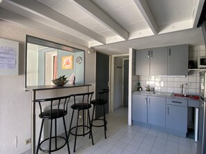 Eine moderne Küche mit grauen Schränken, einer weißen Arbeitsplatte und einer kleinen Kochinsel mit Hockern.