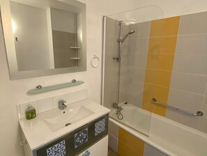 A bathroom with a sink, mirror, shower, and tiled walls.