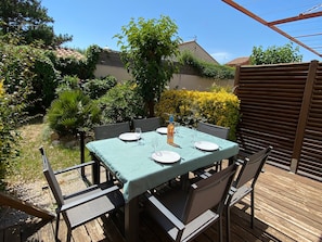 Une terrasse extérieure avec une table dressée pour quatre personnes, entourée de chaises, et une plateforme en bois.