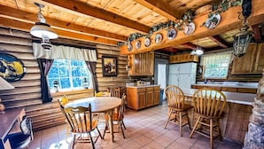 A rustic cabin interior with a wooden dining table, chairs, a kitchen area, and a large window. - Off-grid Cabin at Angel Valley Ranch (Duck Creek Village)