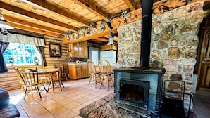 A cozy cabin interior with a stone fireplace, wooden furniture, and a kitchen area. - Off-grid Cabin at Angel Valley Ranch (Duck Creek Village)