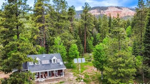 A house surrounded by dense forest with solar panels on the roof. - Off-grid Cabin at Angel Valley Ranch (Duck Creek Village)