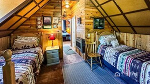 A cozy attic bedroom with two beds, a fireplace, and a wooden ceiling. - Off-grid Cabin at Angel Valley Ranch (Duck Creek Village)