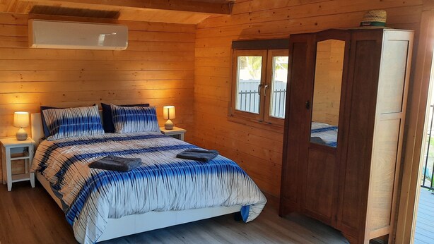 A wooden cabin bedroom with a bed, bedside lamps, and a wardrobe.
