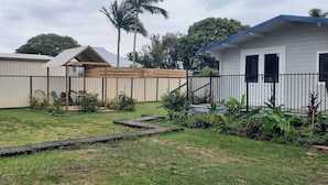 A residential backyard with a wooden deck, a small garden area, and a white house with a blue roof.
