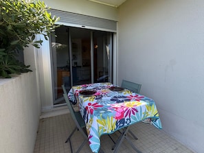 A dining table with a floral tablecloth, a chair, and a view of a kitchen through a sliding glass door. - Studio in Saint Cyprien 50m from the beach (Saint-Cyprien)