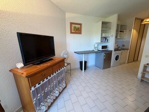 Un ambiente compatto con una televisione su un mobile in legno, un angolo cottura completo di microonde e lavatrice, e un piccolo spazio dedicato alla ristorazione.
