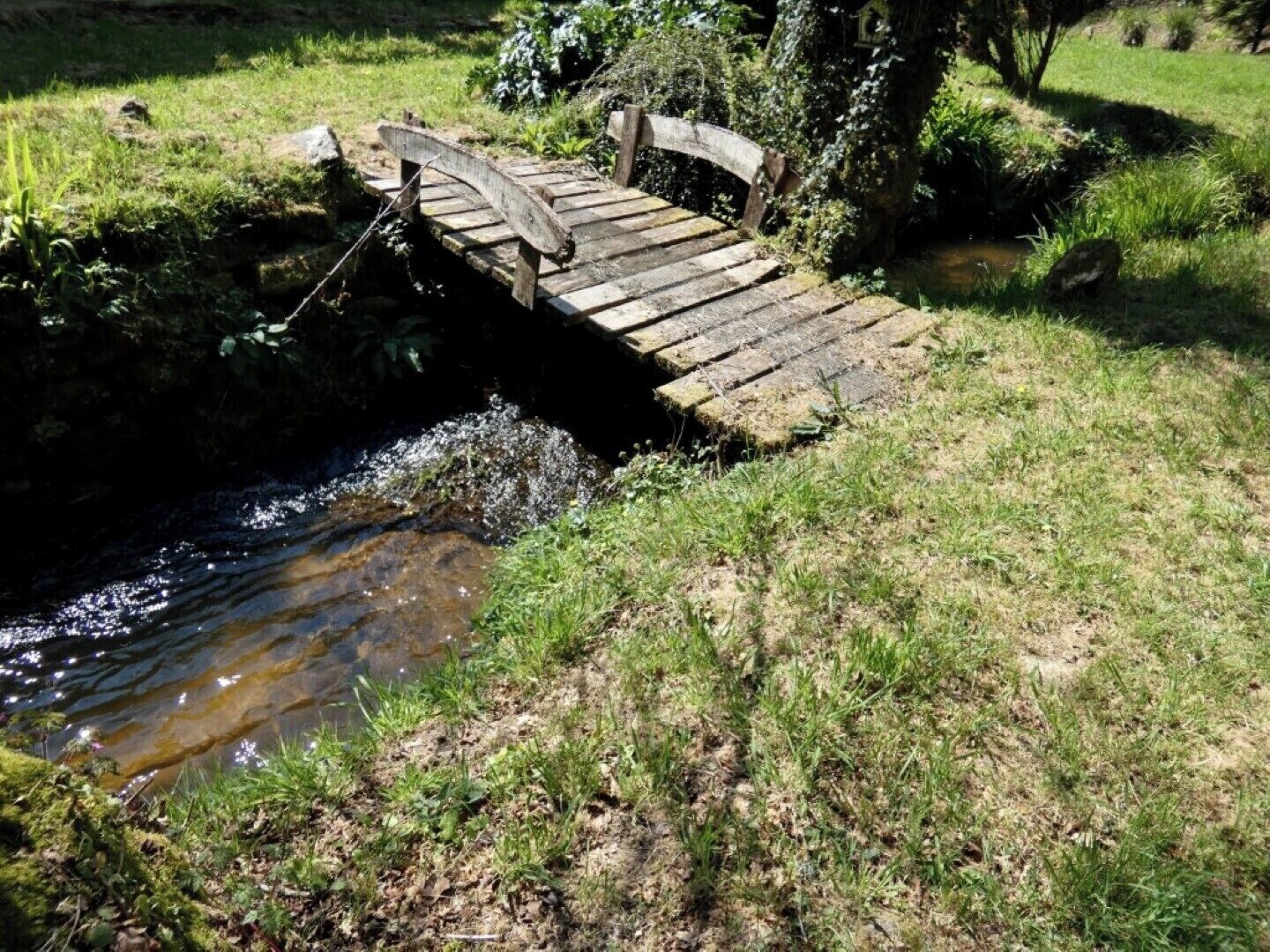 A rustic wooden bridge over a small stream in a natural setting.