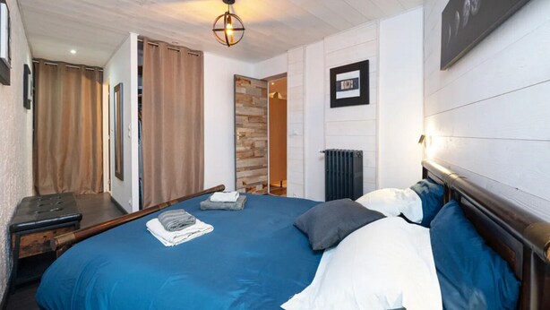 Une chambre avec un grand lit, une tête de lit en bois, un luminaire suspendu, un radiateur et un tableau accroché au mur.