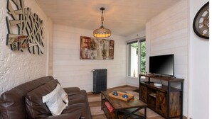 Un salon chaleureux avec un canapé en cuir, une table basse en bois, un téléviseur posé sur un meuble en bois et un grand tableau abstrait accroché au mur.
