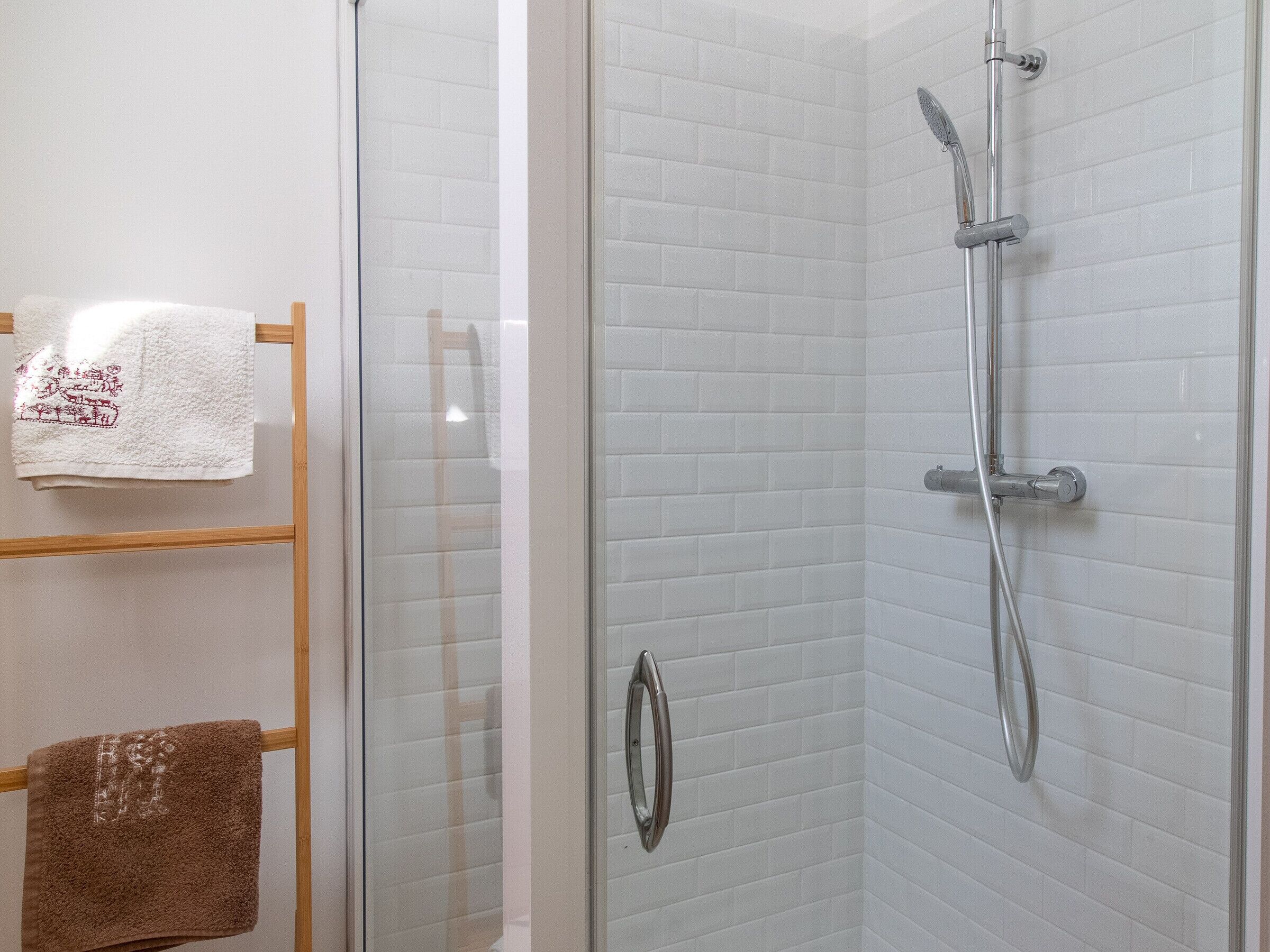 A glass-enclosed shower with a handheld showerhead and a wall-mounted faucet.