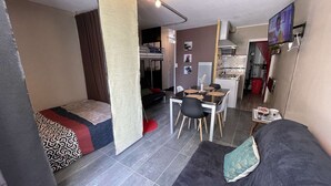 Un espace de vie compact comprenant un canapé, une table à manger avec des chaises, un coin cuisine et un petit espace aménagé pour dormir.