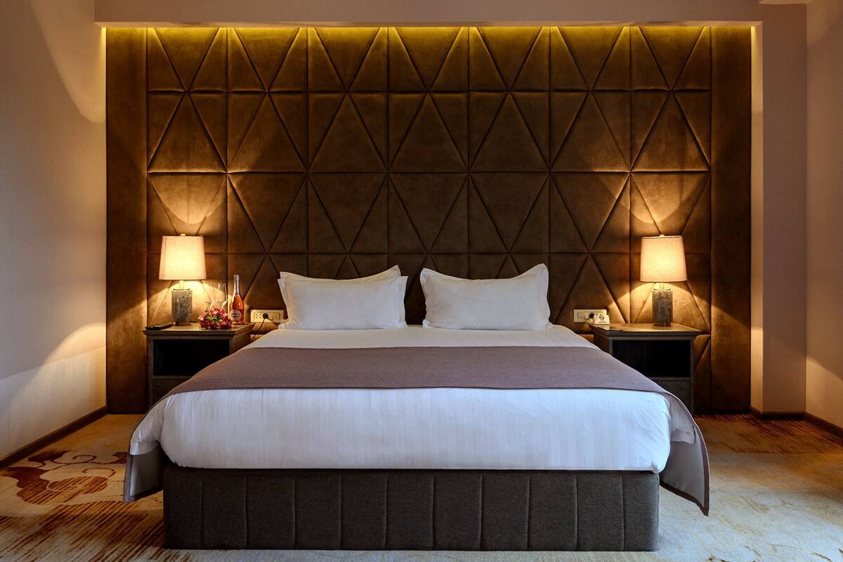 A hotel room with a large bed, two bedside tables, and a decorative headboard.