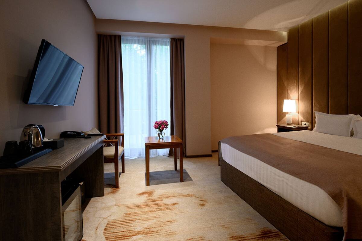 A hotel room with a bed, a desk, a chair, a TV, and a window with curtains.