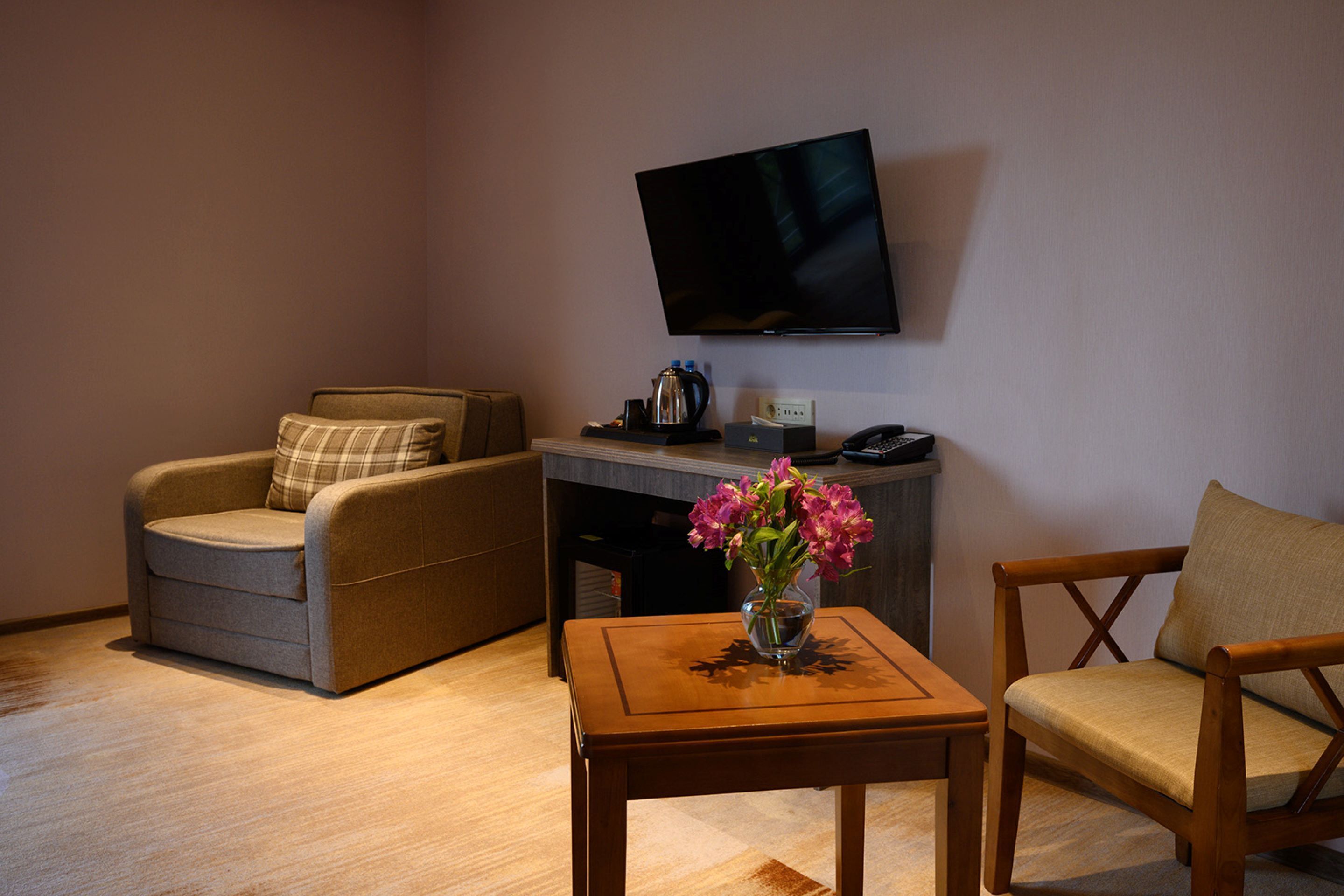 A living room with a sofa, armchair, coffee table, and a flat-screen TV mounted on the wall.