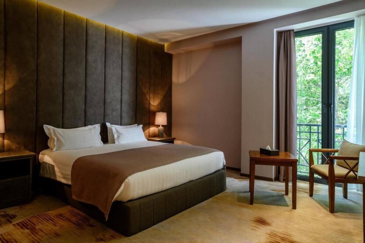 A hotel room with a large bed, bedside tables, a chair, and a balcony with a view.