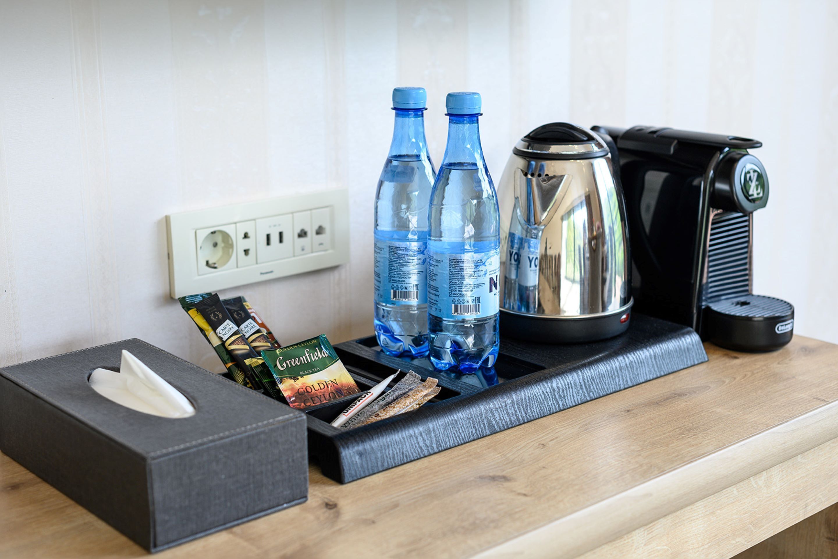 A hotel room's minibar with bottled water, coffee maker, tea bags, and a tissue box.