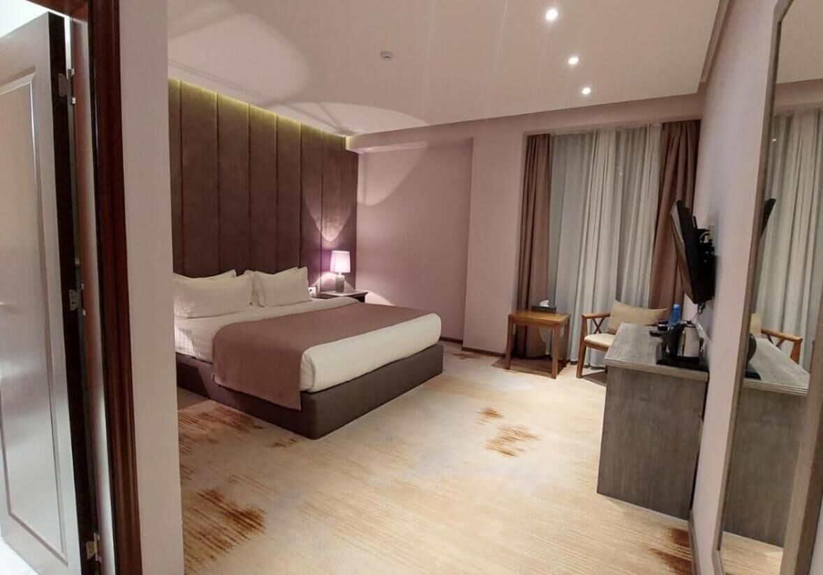Une chambre d’hôtel moderne, dotée d’un grand lit, d’une table de chevet, d’une lampe et d’un petit bureau avec une chaise.