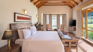 A hotel room with a large bed, a TV, a sofa, and a desk. There is a window with curtains and a view of greenery outside. - Welcomhotel By ITC Hotels Hamsa Manali (Manali)