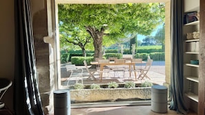 Une pièce avec une grande fenêtre, une table en bois avec des chaises, une bibliothèque et une petite table ronde.