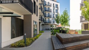 A modern apartment building with balconies, a paved walkway, and wooden seating areas. - Cozy Apartment | Garage Parking and Balcony (Poznan)