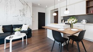 A modern living room with a dark sofa, a white coffee table, and a dining area with a wooden table and black chairs. - Cozy Apartment | Garage Parking and Balcony (Poznan)