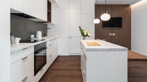 A modern kitchen with white cabinetry, a marble island, and a wooden accent wall. - Cozy Apartment | Garage Parking and Balcony (Poznan)