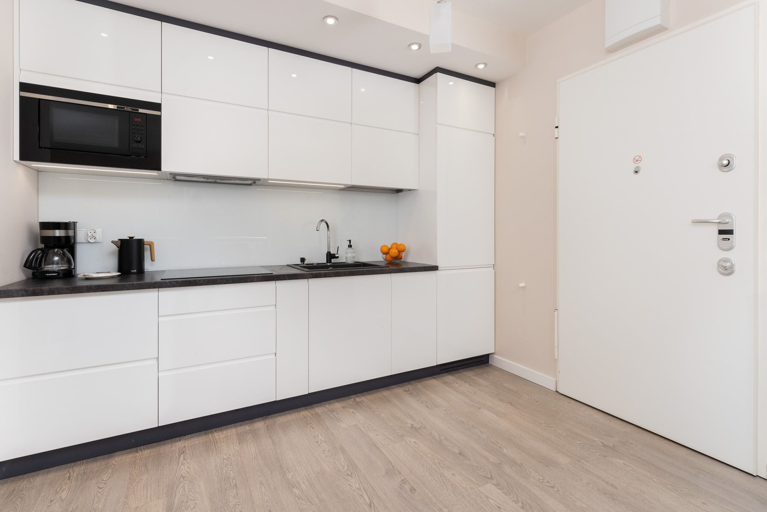 A modern kitchen with white cabinets, a black microwave, a coffee maker, and a sink.