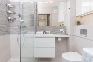 Un baño moderno con ducha envuelta en vidrio, un lavamanos blanco y un inodoro.