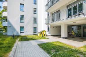 Un edificio de apartamentos moderno con un camino pavimentado, un pequeño área de juegos y bicicletas estacionadas afuera.
