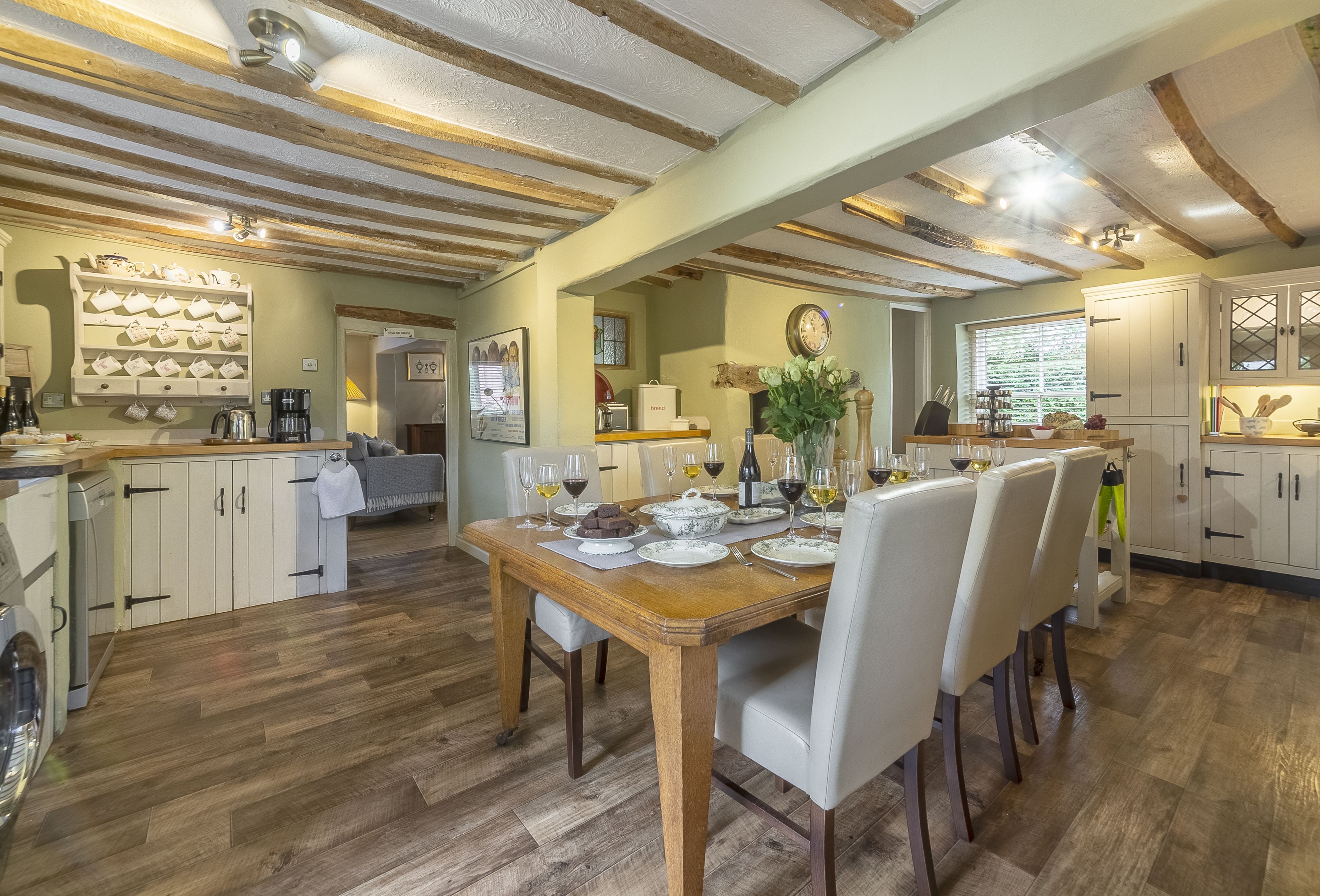 A dining area with a wooden table set for a meal, surrounded by white chairs.