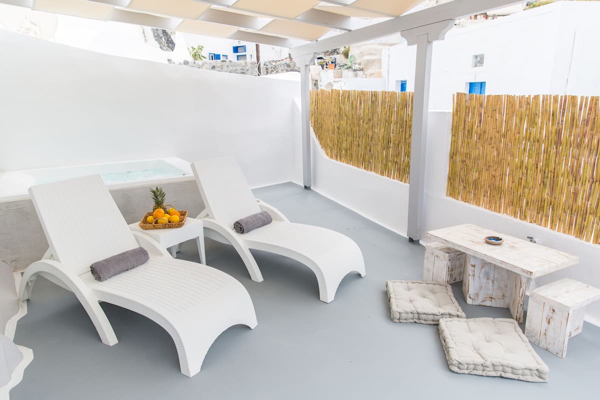 A sunlit outdoor seating area with two white lounge chairs, a small table, and a bamboo fence.