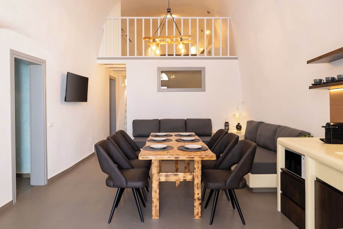 A dining area with a wooden table and black chairs, a sofa, a TV, and a staircase.