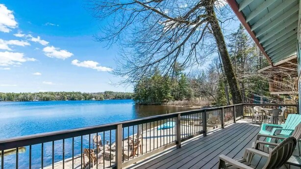 Une terrasse en bois avec des chaises et une table, donnant sur un lac.