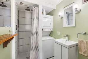 Un bagno con doccia, lavatrice e asciugatrice integrate, lavabo e specchio.