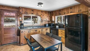 Une cuisine aménagée dans le style d’un chalet en bois, avec une table et des chaises, un réfrigérateur noir et des placards en bois.