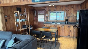 Une petite cabane en bois comprenant un coin cuisine, un espace repas et un canapé.