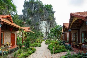 A courtyard with brick buildings, a central pathway, and a large rock formation in the background. - Rubyhomestay (Nam Hoa Lu)