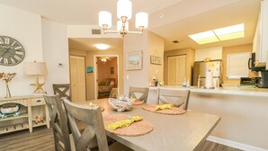 A dining area with a wooden table, four chairs, a chandelier, and a clock on the wall.