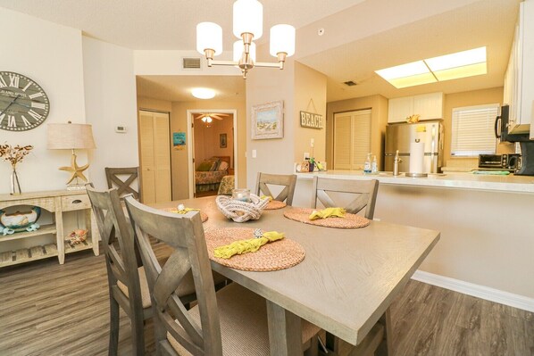A dining area with a wooden table, four chairs, a chandelier, and a clock on the wall.