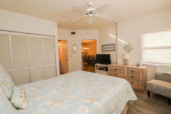 A bedroom with a bed, a dresser, a television, a ceiling fan, and a window with blinds.