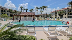 A pool area with lounge chairs, palm trees, and a covered pavilion.