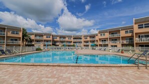 A swimming pool with lounge chairs, a tiled deck, and a multi-story building with balconies. - Enjoy the Sunrise and the Sunset from your very own Balcony! (St. Augustine)