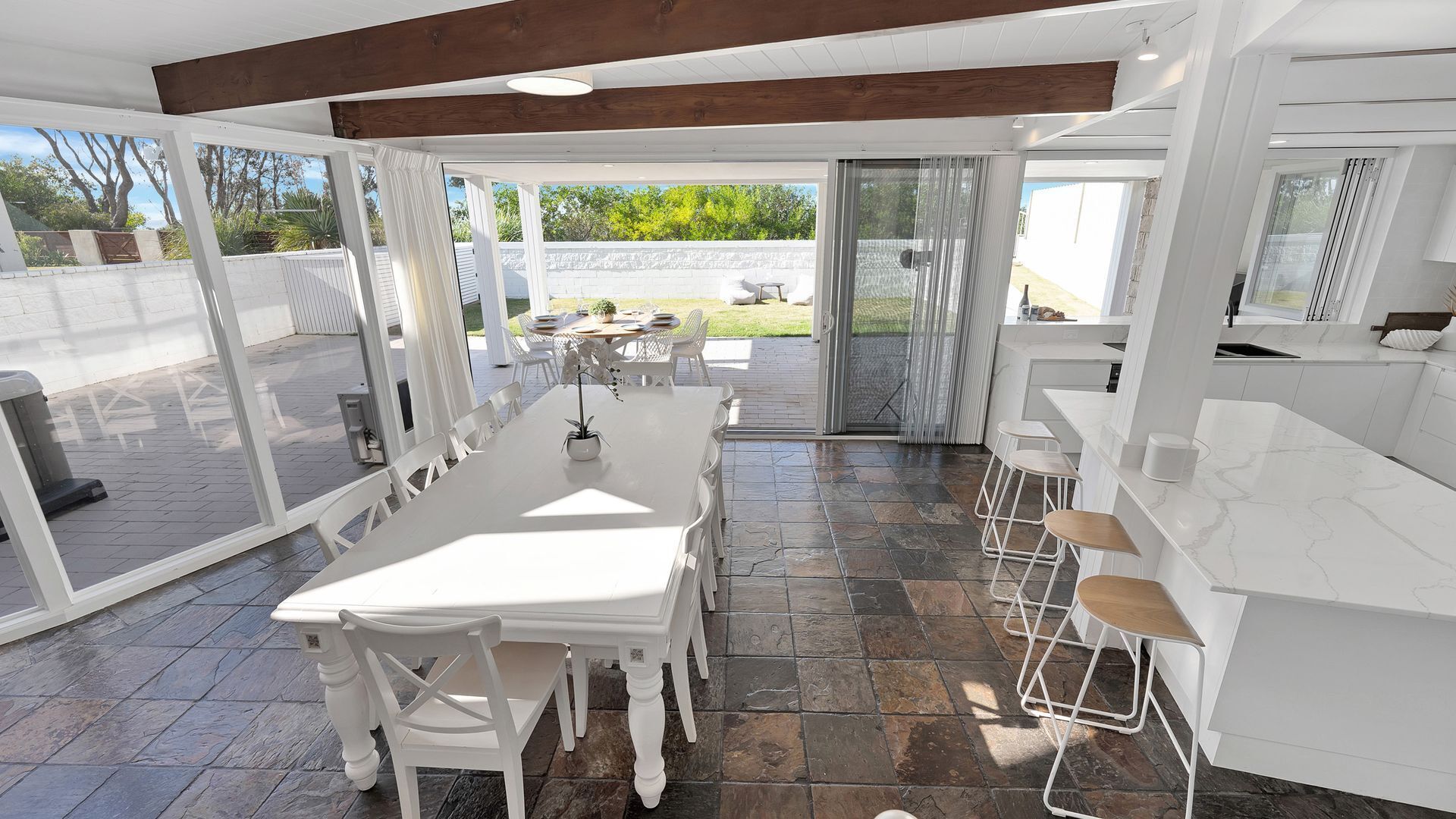 Un patio amplio con una mesa y sillas de comedor, una zona de cocina con taburetes de bar y una puerta corrediza de vidrio que da a un espacio exterior.