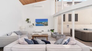 A modern living room with a sofa, coffee table, and a painting of a coastal landscape. - Ubuntu by Experience Jervis Bay (Vincentia)