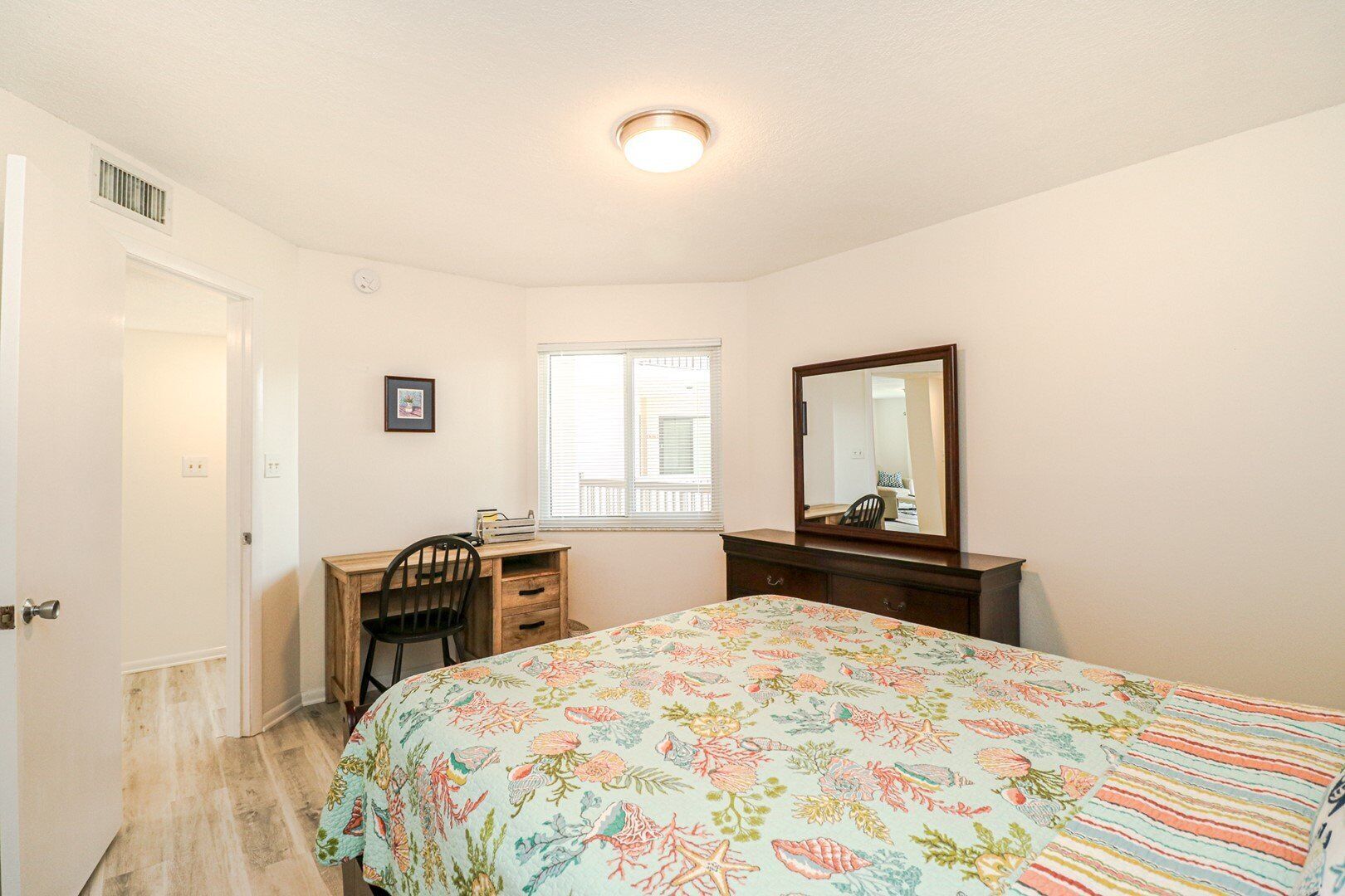 Une chambre à coucher comprenant un lit, un bureau, une chaise, une commode, une fenêtre et un miroir.